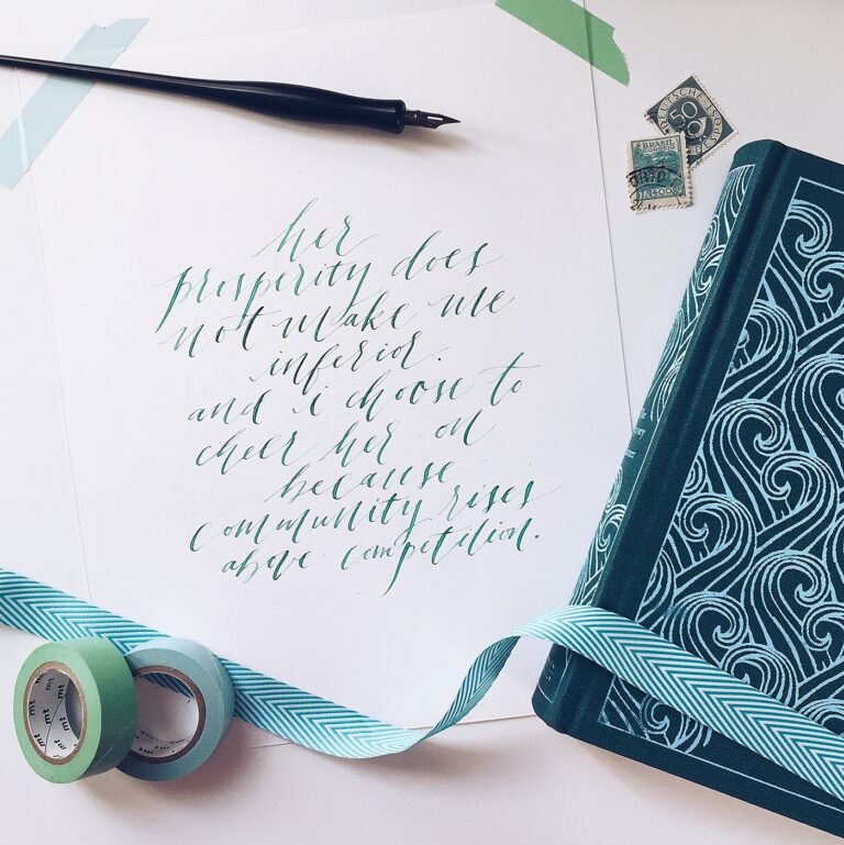 Calligraphy on a piece of paper taped to a surface, surrounded by washi tape, stamps, and a book