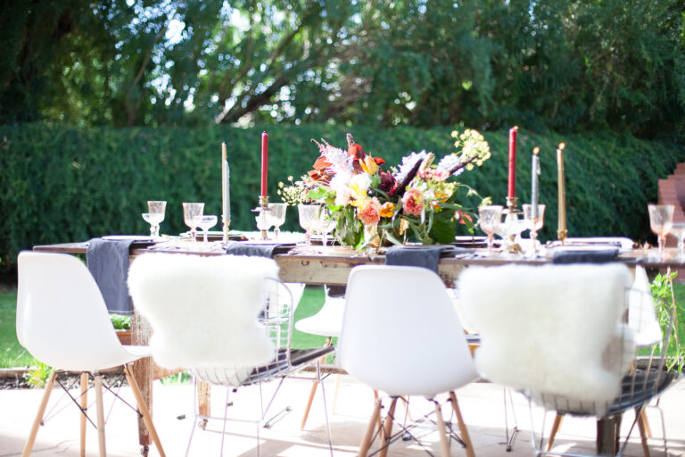 A dining table outside set with candles and a floral centerpiece.