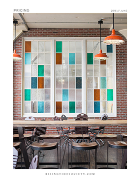 A long wooden table with chairs in front of a brick wall with a color-blocked glass window