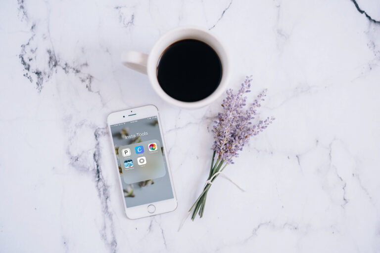 An iPhone, cup of coffee, and small bouquet of lavender on a marble surface