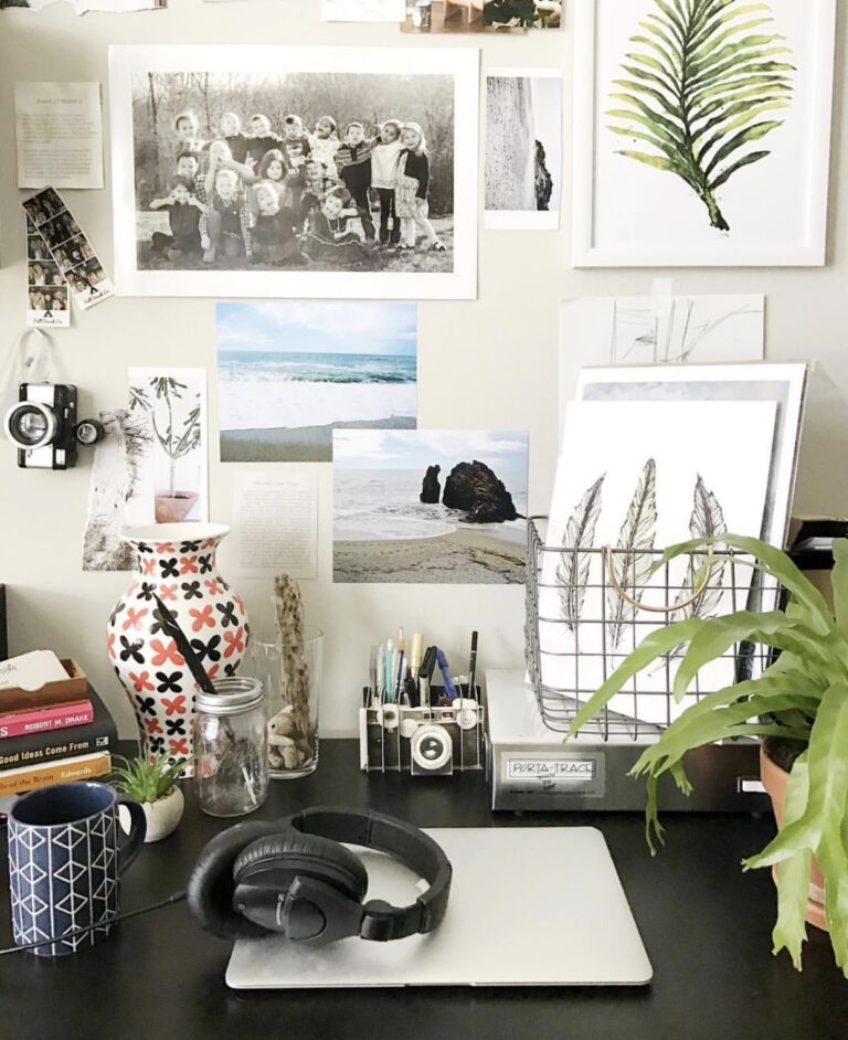 An organized desk set with books, a plant, and accessories. An assortment of art hangs on the wall.