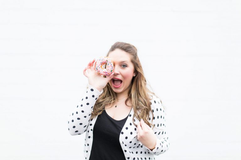 Woman holding a pink sprinkled donut to her eye.