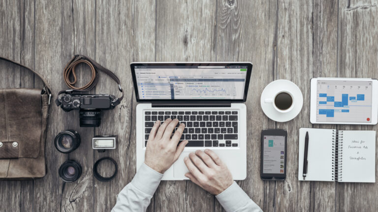 Aerial view of hands working at a laptop surrounded by camera equipment and other work supplies