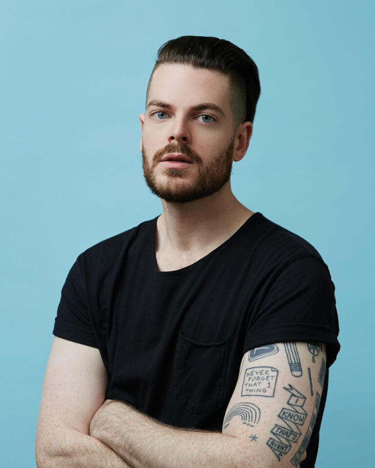 A headshot of a man in front of a blue backdrop.