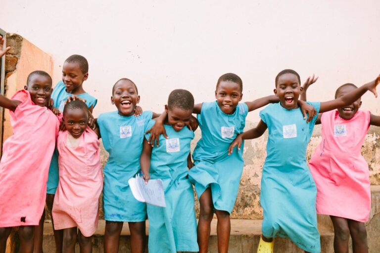 A group of children in colorful uniforms jump and smile together.