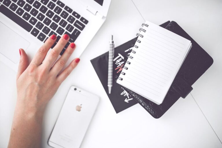 Close up of a hand working at a table next to a notebook and an iPhone.