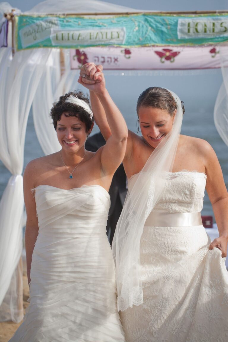 Newly wed brides lift their arms together in celebration