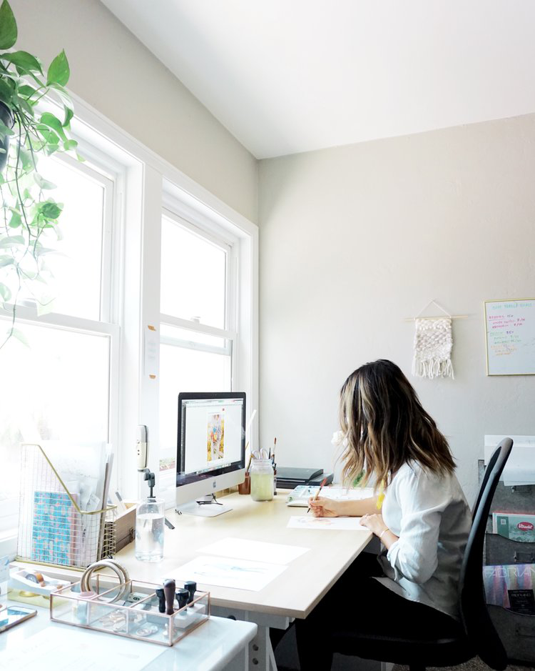 A woman works in a brightly lit office in front of a pair of white windows