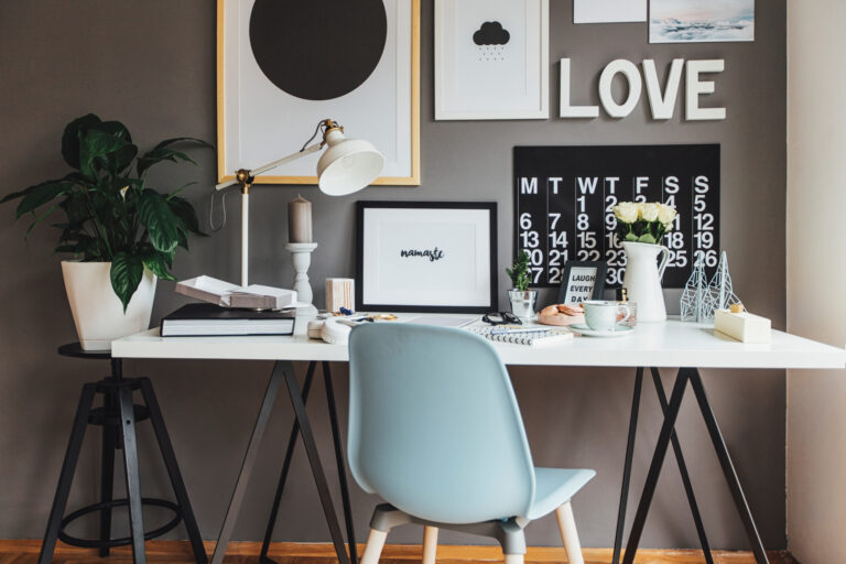 A white desk styled with art and accessories against a dark wall