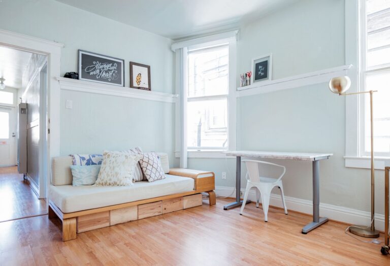 A brightly lit room with wooden floors, a daybed, and desk.