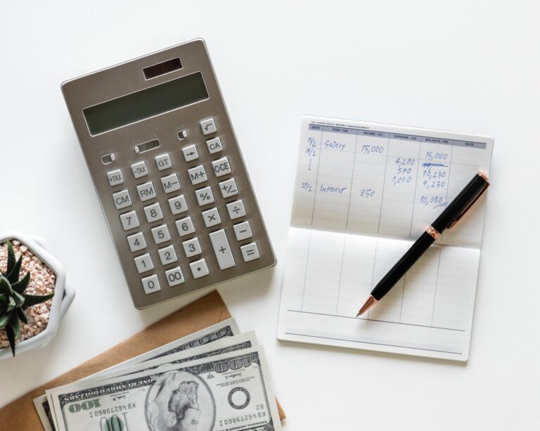 A calculator, checkbook, and stack of one hundred dollar bills on a white surface