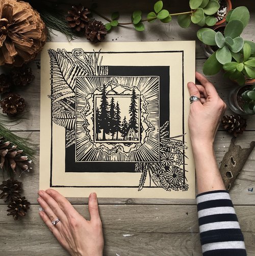 A pair of hands hold an ink drawing, surrounded by plants and acorns.