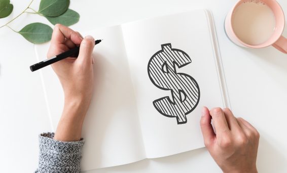 Top down view of woman drawing a dollar sign symbol in a notebook.