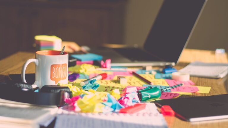 Desk full of crumpled post-its, paper, and a coffee mug.