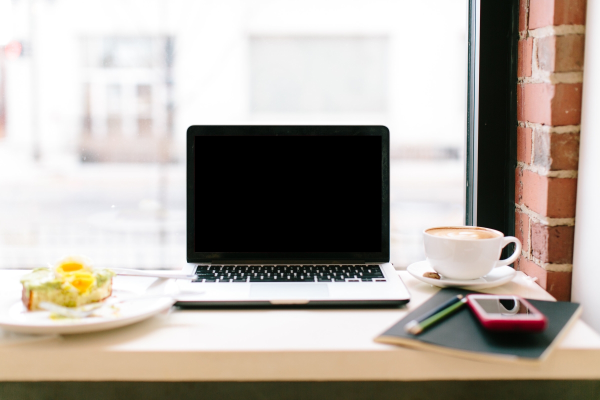 Computer sitting on a table in a coffee shop facing a window