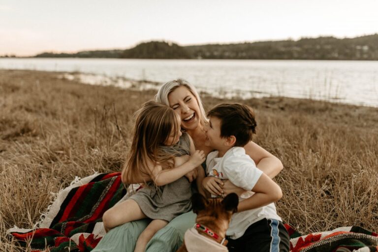 Young mom hugging and tickling her two kids in a field.