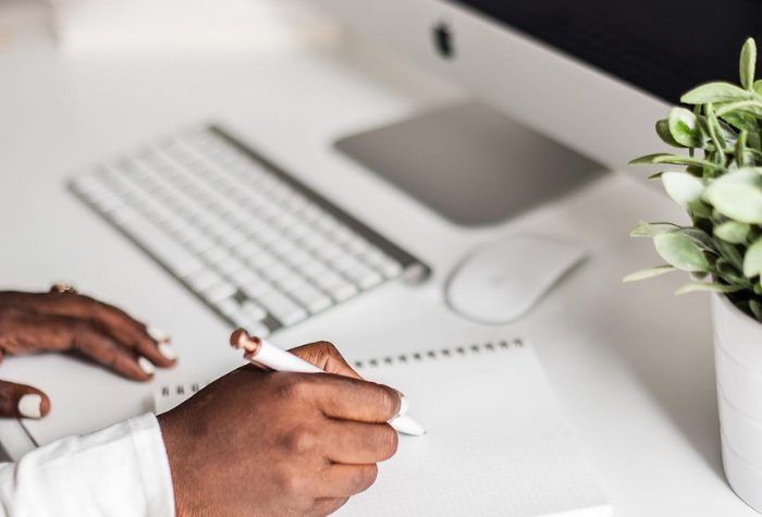 Woman's hands holding a pen on paper beside a white and silver mac computer.