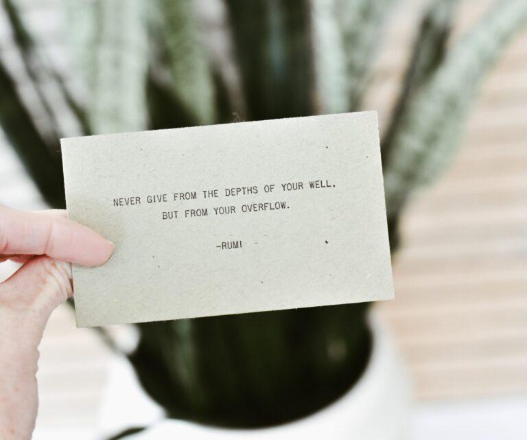 Close up of a card with a Rumi quote, held in front of a potted plant
