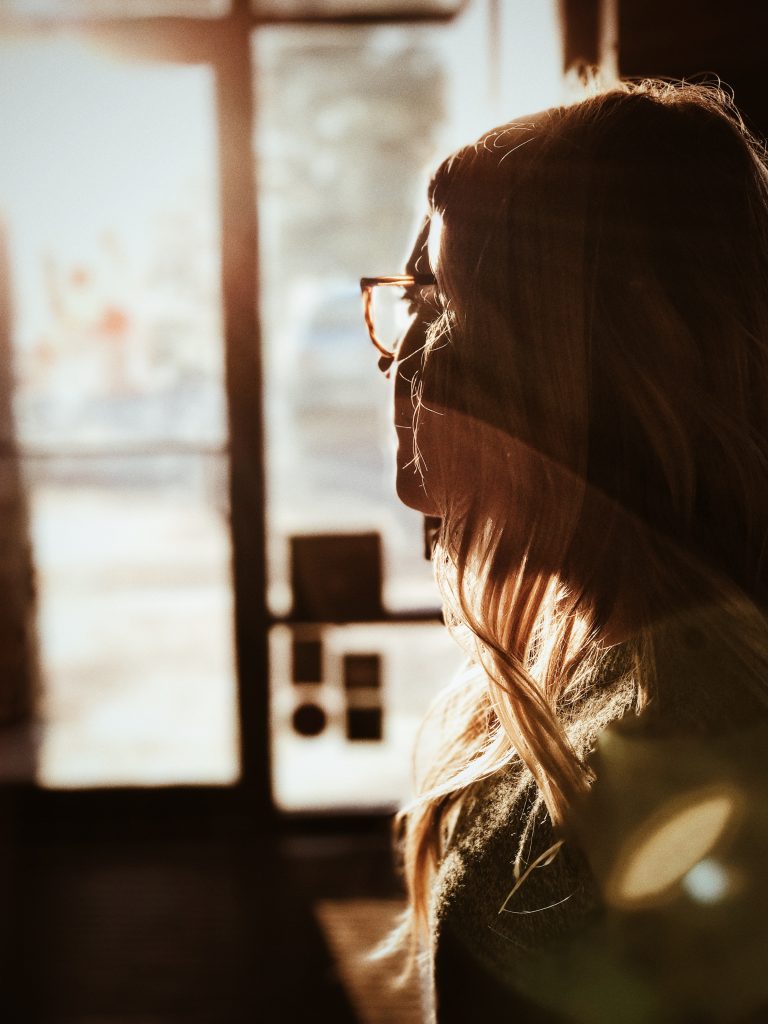 Woman with glasses looking out of a sunny window.