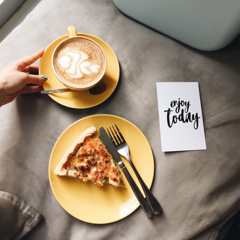 A hand places a latte next to a slice of savory pie and a note stating 