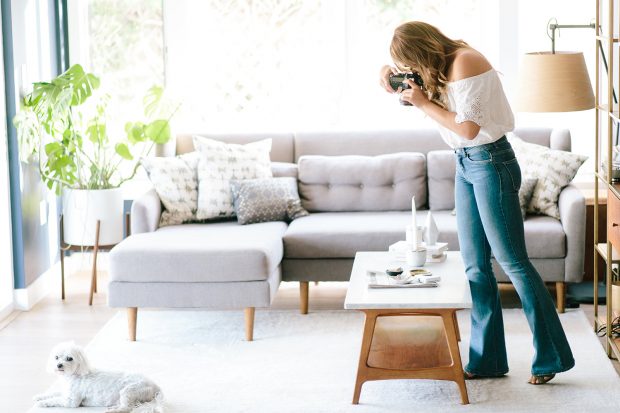 woman in a living room pointing her camera down at a setting on a coffee table