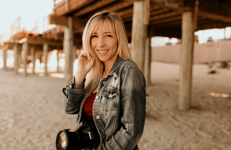 woman holding a camera on the beach in front of a pier