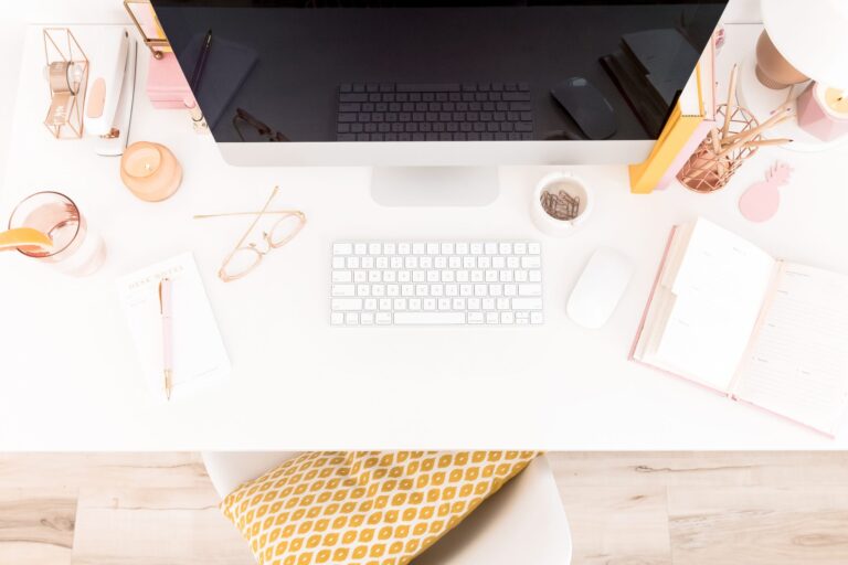 Aerial view of a white desk styled with assorted pink accessories and an iMac with keyboard.