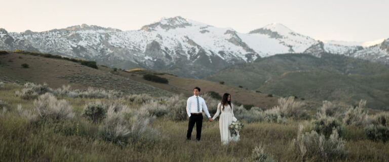 a bride and groom holding hands posing in front of a mountain