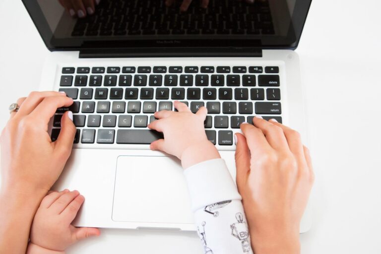 Close up of woman's hands typing on a laptop with baby in lap.