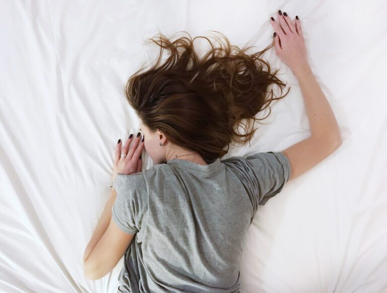 woman in a grey shirt laying on a white bedsheet