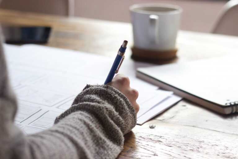 a person writing at a desk with coffee in the background