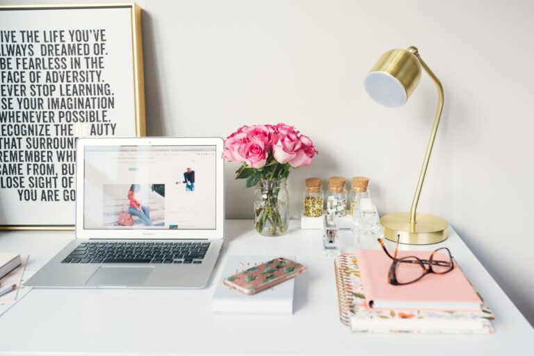 an open laptop on a desk decorated with flowers and a lamp