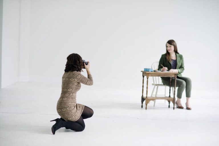 photographer taking a photo of a woman posed at a desk