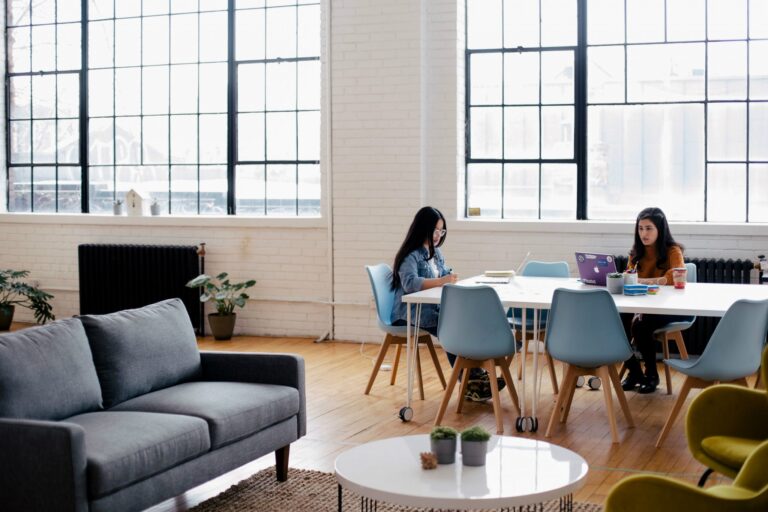 Two women work at a table in a large, loft space.