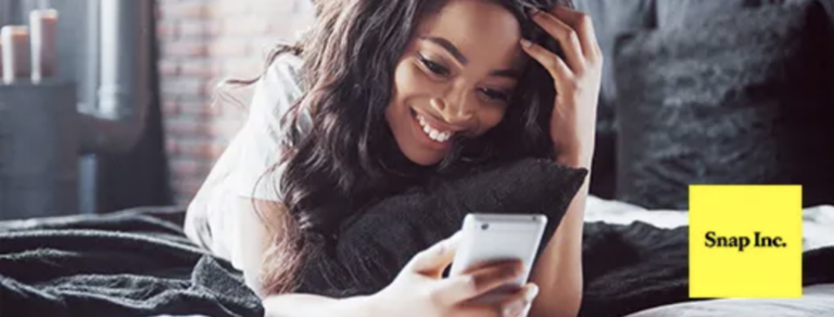 a smiling woman on a bed looking at her smartphone with the Snap, Inc. logo in the corner