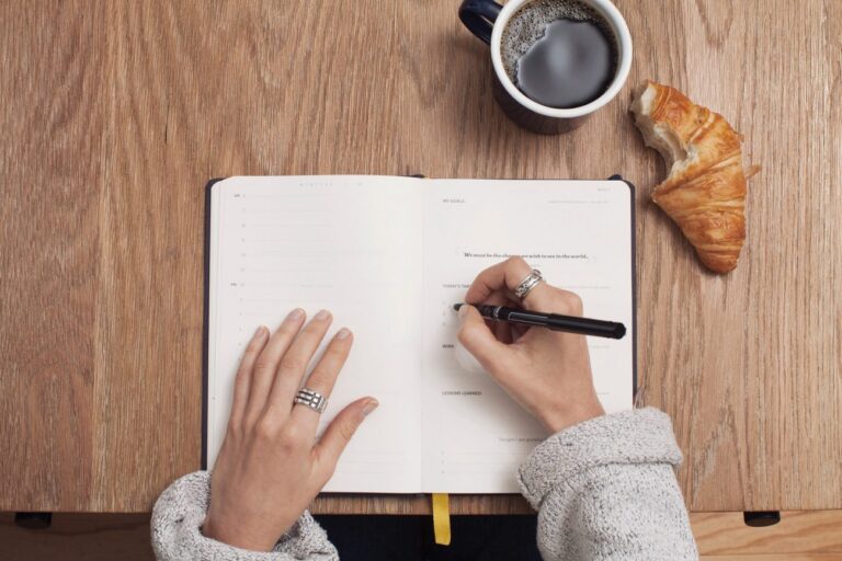 a woman writing goal setting questions in an open notebook on a wood desk