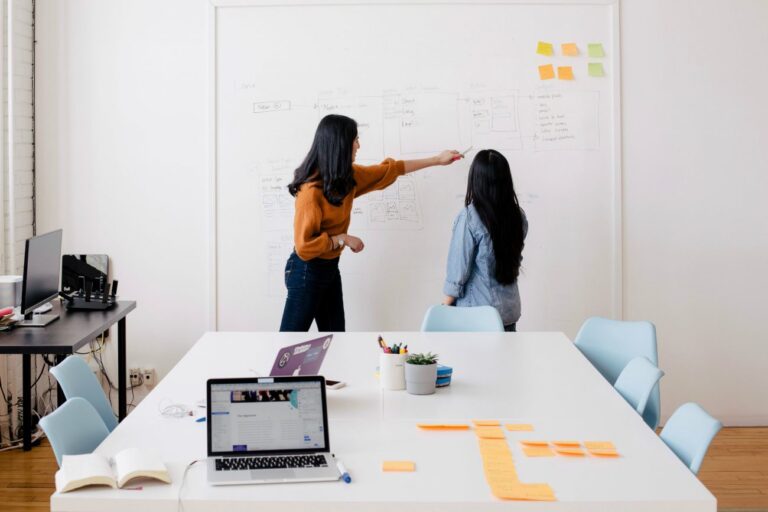 Two young female entrepreneurs write a business plan on a whiteboard.