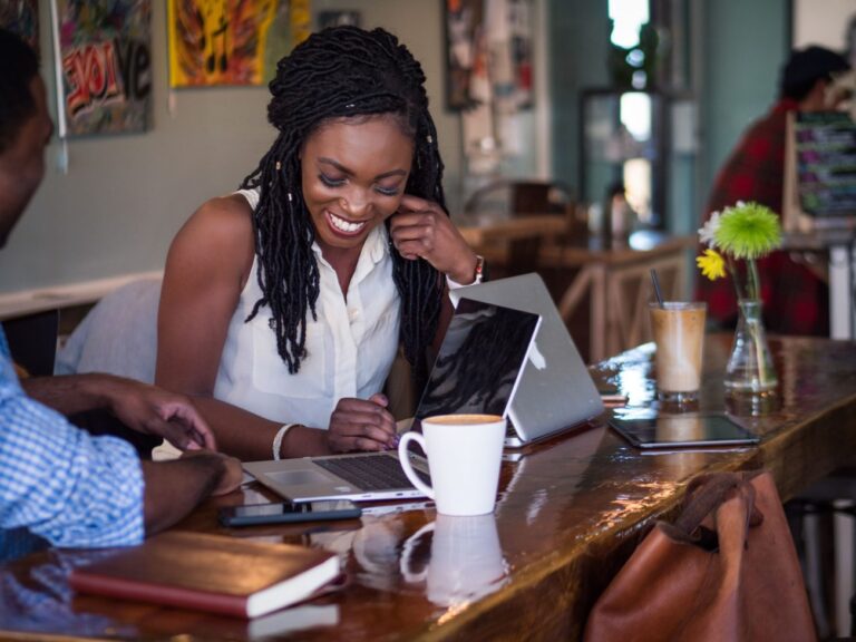 a man and woman talking in front of a laptop and cup of coffee in a cafe