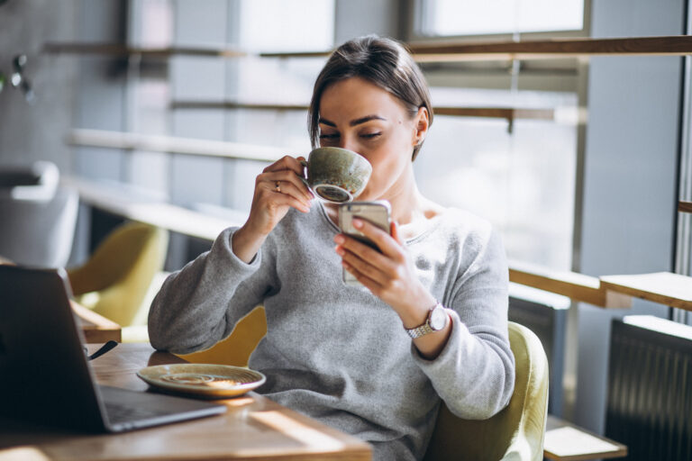 A woman drinks from a mug as she looks at her phone.