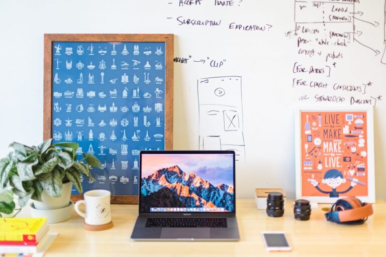 a desk scene with a laptop, coffee mug, poster and whiteboard