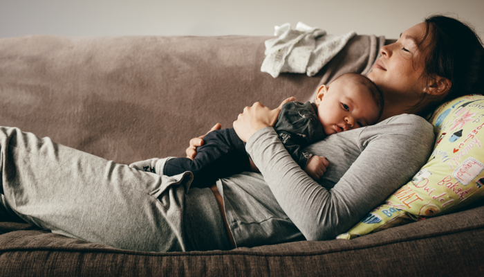 a mom laying on her back on a couch with her baby laying on her stomach