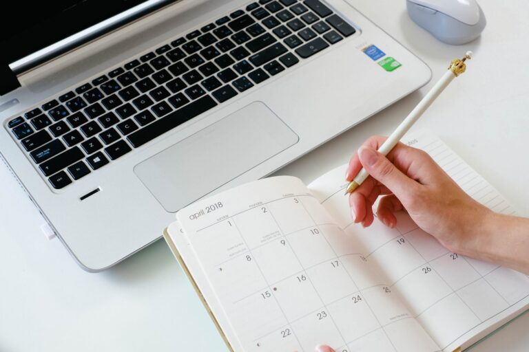 Close up of a hand writing in a planner in front of an open laptop