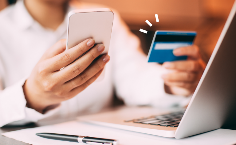 a woman at a laptop holding a credit card and smartphone