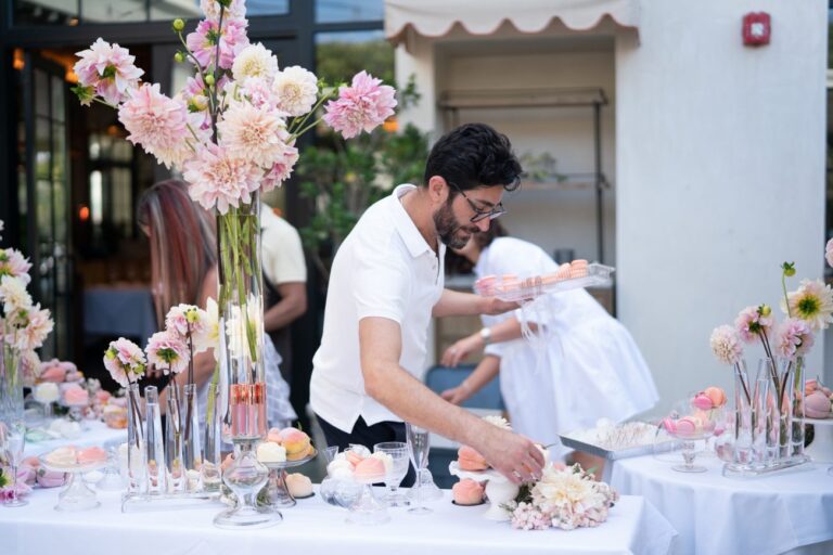 a man holding a tray of macaroons setting a table with flowers on it