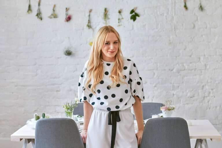 Pretty blonde elegant Caucasian woman standing by the dining table and looking at camera.