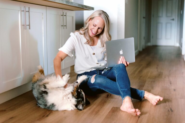 a woman sitting on the floor holding her laptop and petting a dog