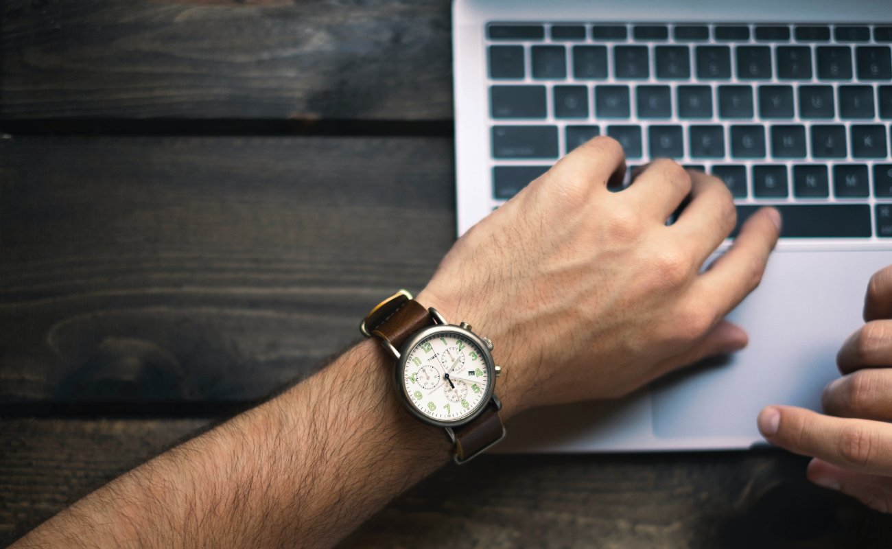 Man's hand on laptop keys showing watch for time tracking