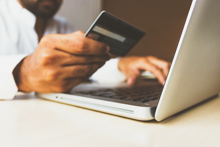 a man holding a credit card and typing on a laptop