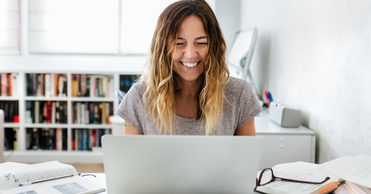 Woman sitting at a table looking down at a laptop and smiling