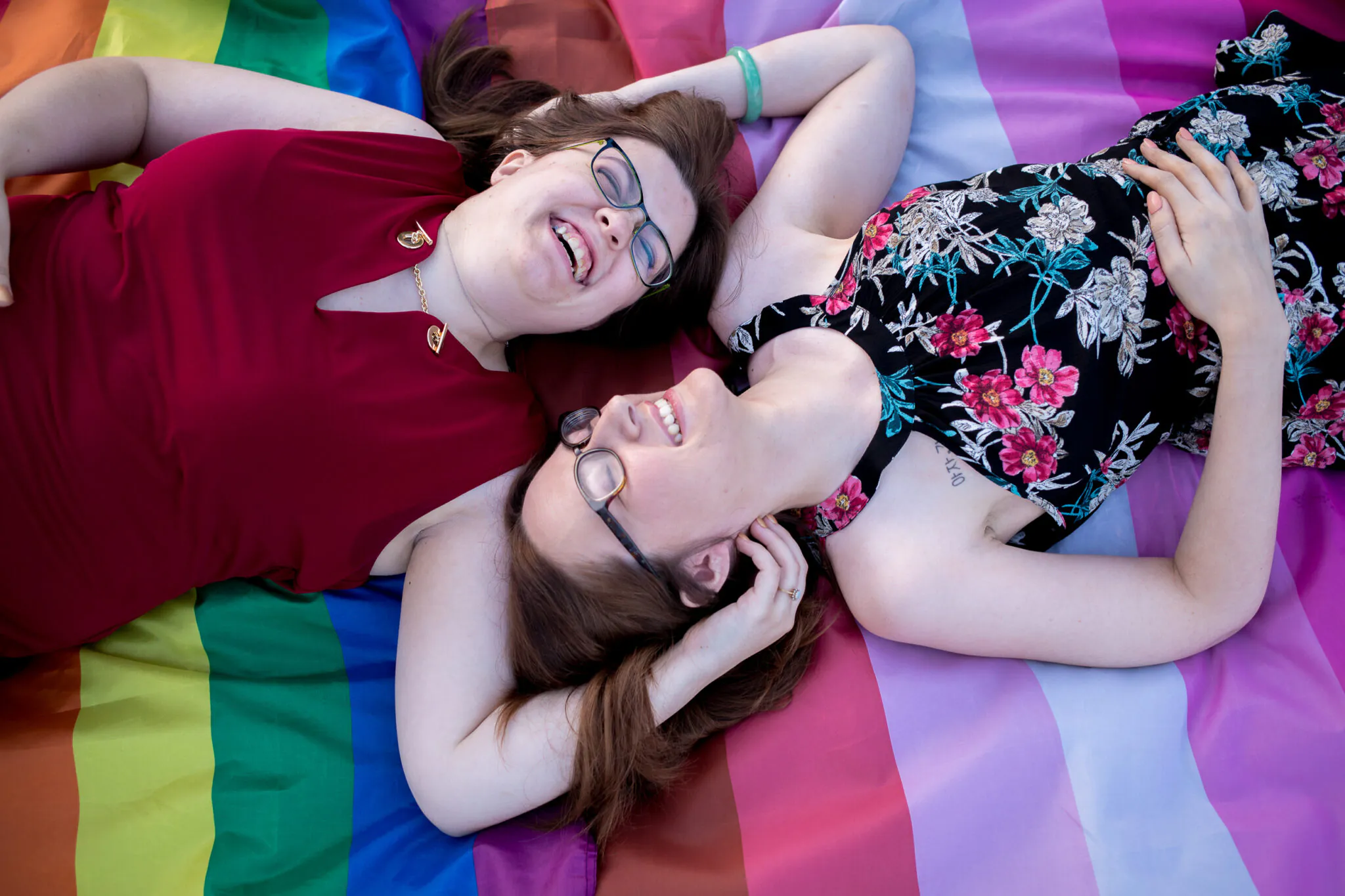 Two women laugh on a rainbow flag